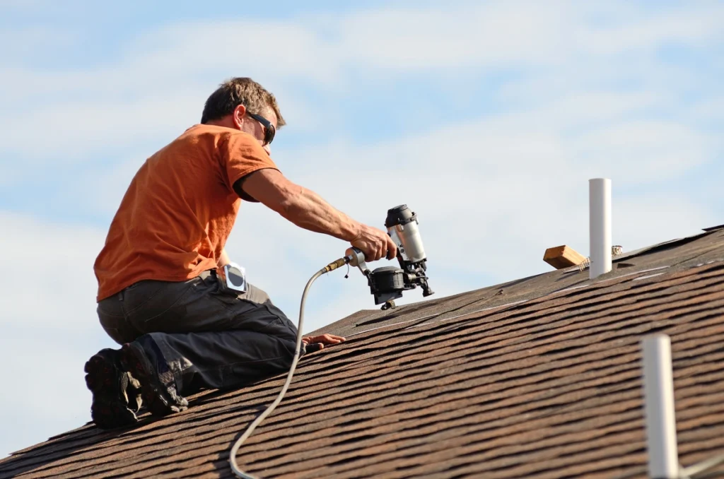 man using nail gun to replace shingles on rooftop